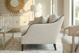 Side profile view of a beige upholstered sofa featuring a curved slope arm outlined with dark wood trim and tapered legs.
